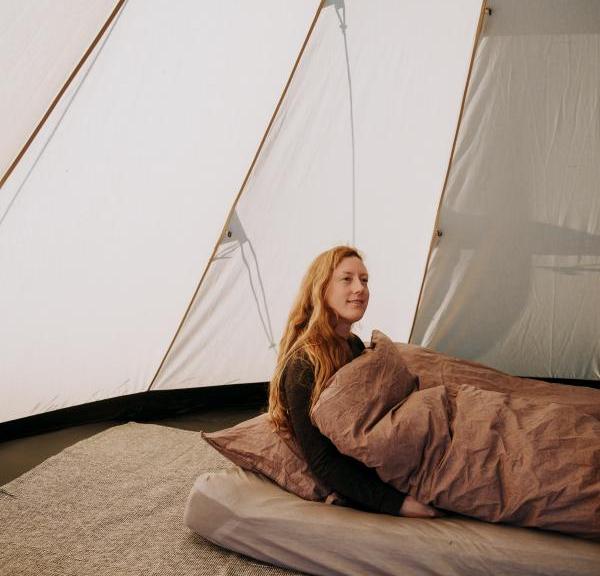 Person sidder i seng inde i glampingtelt og nyder komfortabel overnatning hos Outdoor Adventures.